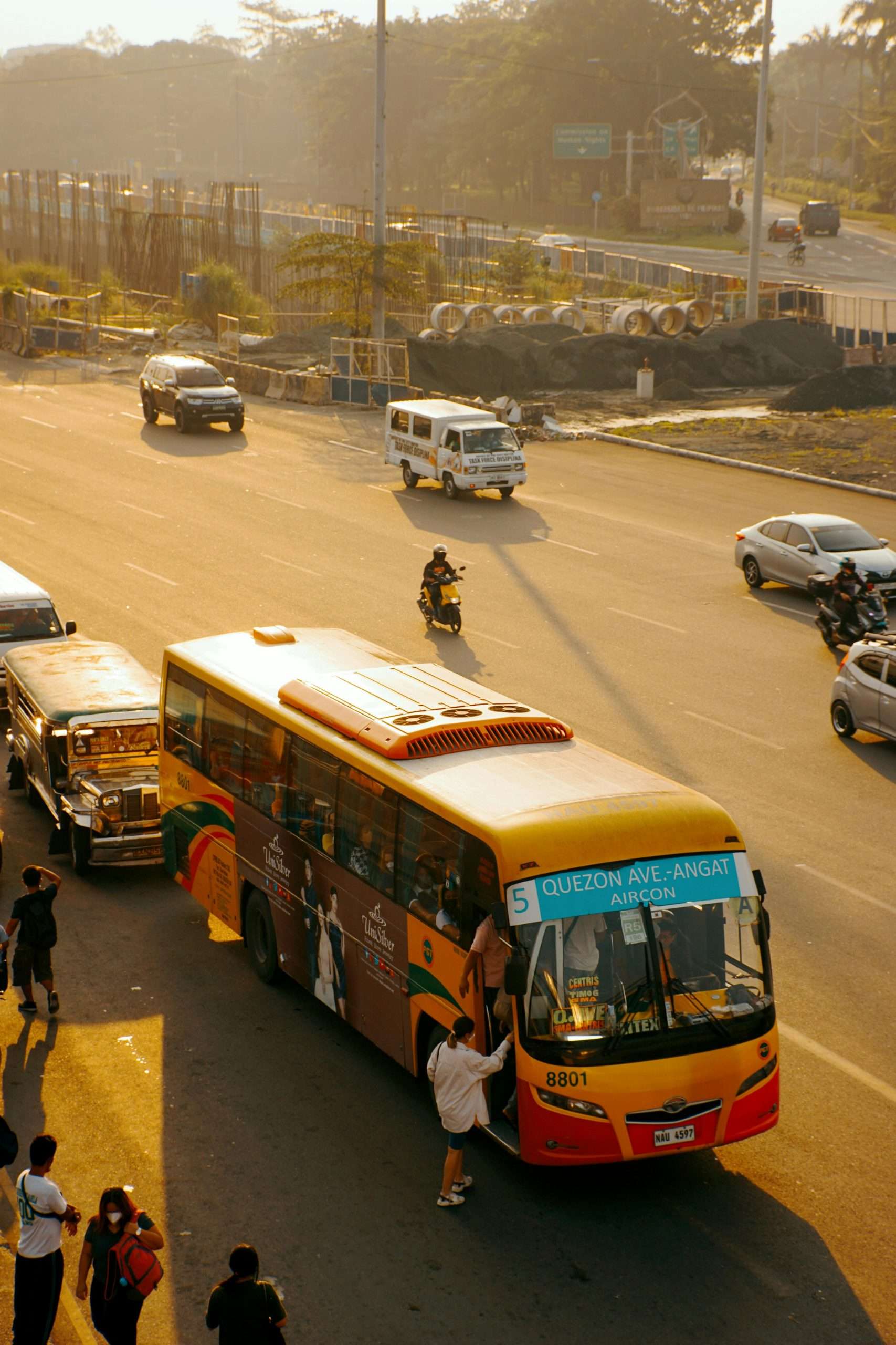 Commuters and vehicles in bustling traffic on Quezon Avenue during sunset.