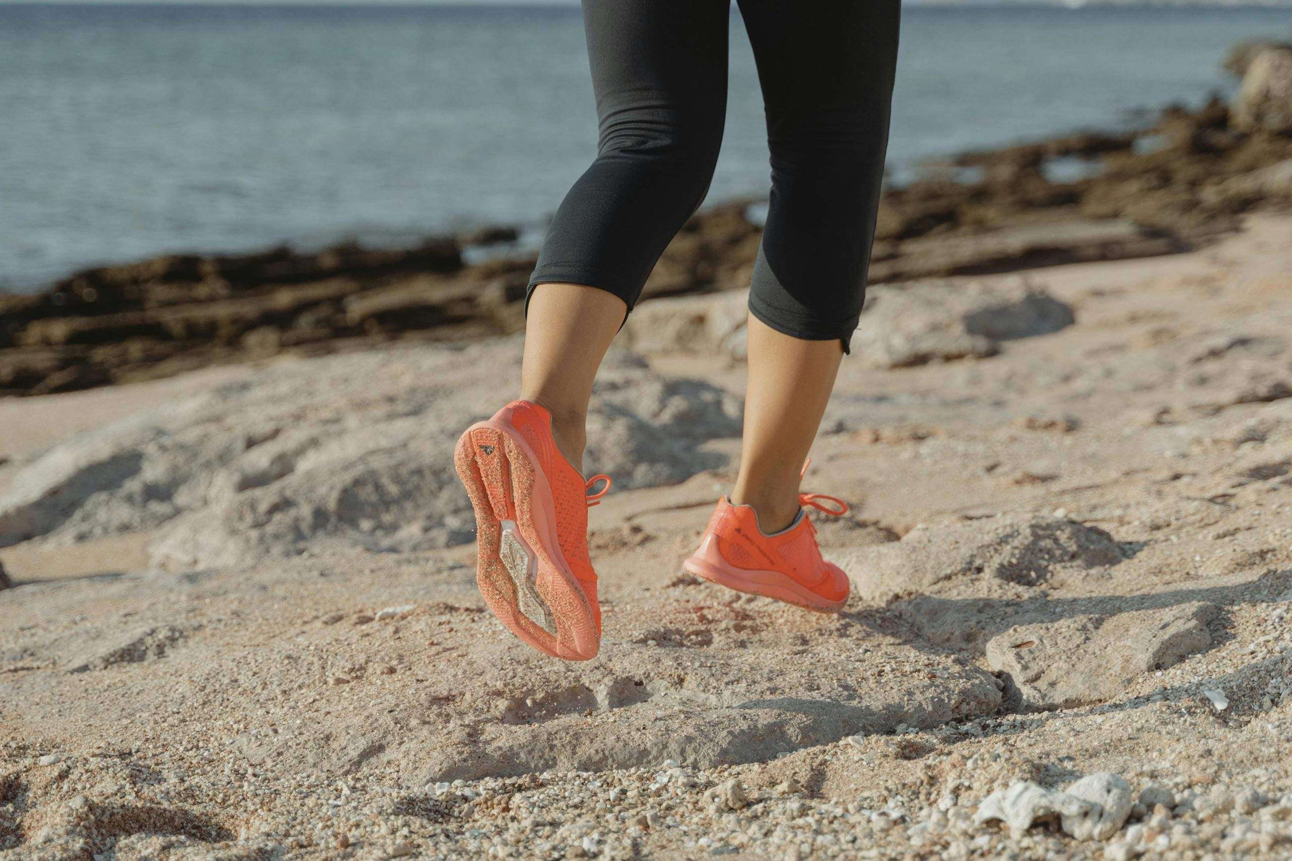 Adult jogging on the beach with vibrant orange shoes, showcasing active lifestyle.